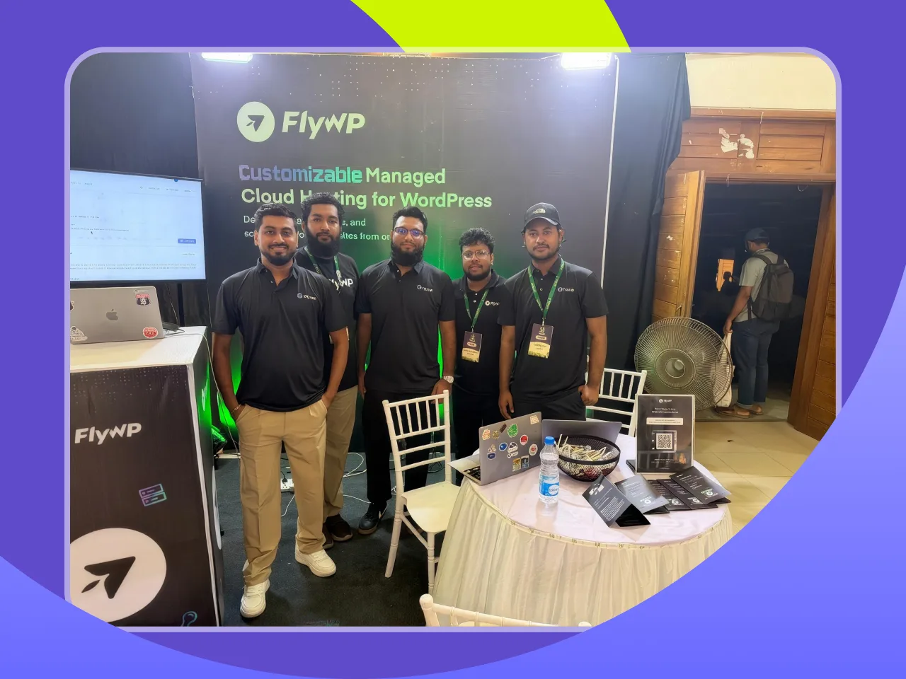 Five FlyWP team members in black polos standing together in front of the FlyWP booth banner