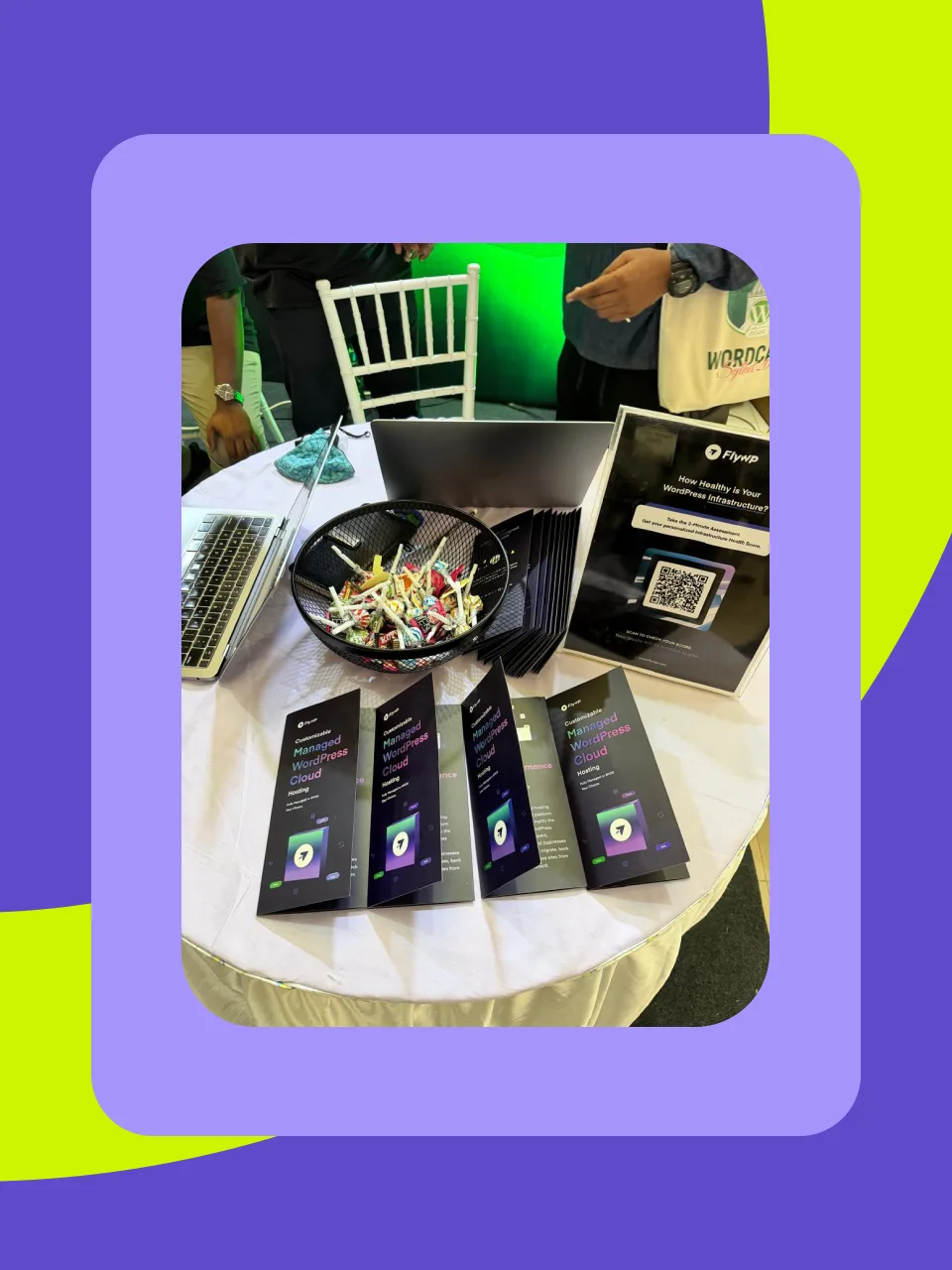 A bowl of lollipops on the booth table next to FlyWP brochures and a QR code card for the infrastructure health assessment
